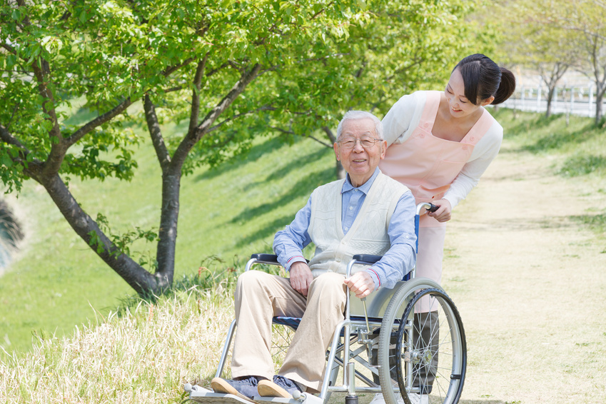Elderly man in a wheelchair with a younger woman assisting him